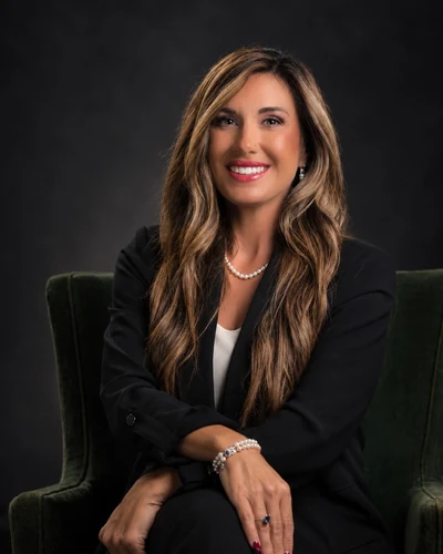 Kristina Popwell, SPHR, CSP, CEO & Founder of Quality Logistic Solutions, seated in a green armchair in a black blazer and pearls, smiling.